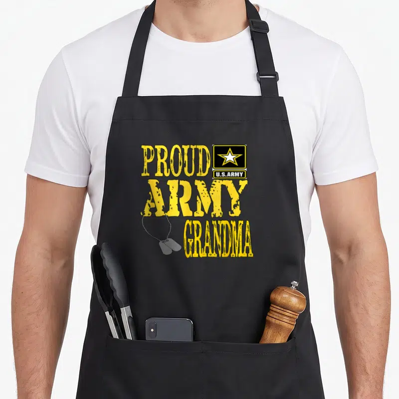 Military grandma apron - Stacked yellow distressed PROUD U.S.ARMY ARMY GRANDMA text with star logo and hanging dog tags — shown on a black cotton canvas apron against a white background