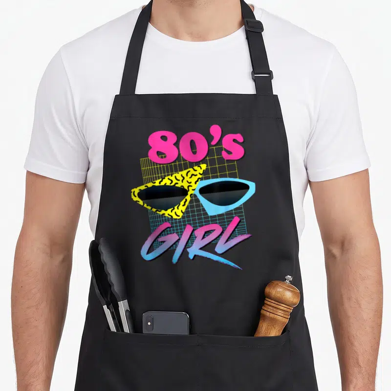 Vintage costume 80s apron - Retro sunglasses with yellow squiggle and blue frames over a grid with 80'S GIRL text — shown on a black cotton canvas apron against a white background