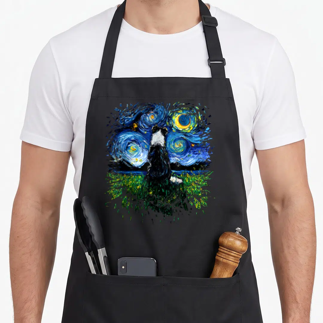 Starry border collie apron - Black and white dog sitting on green grass facing a swirling blue night sky with yellow — shown on a black cotton canvas apron against a white background