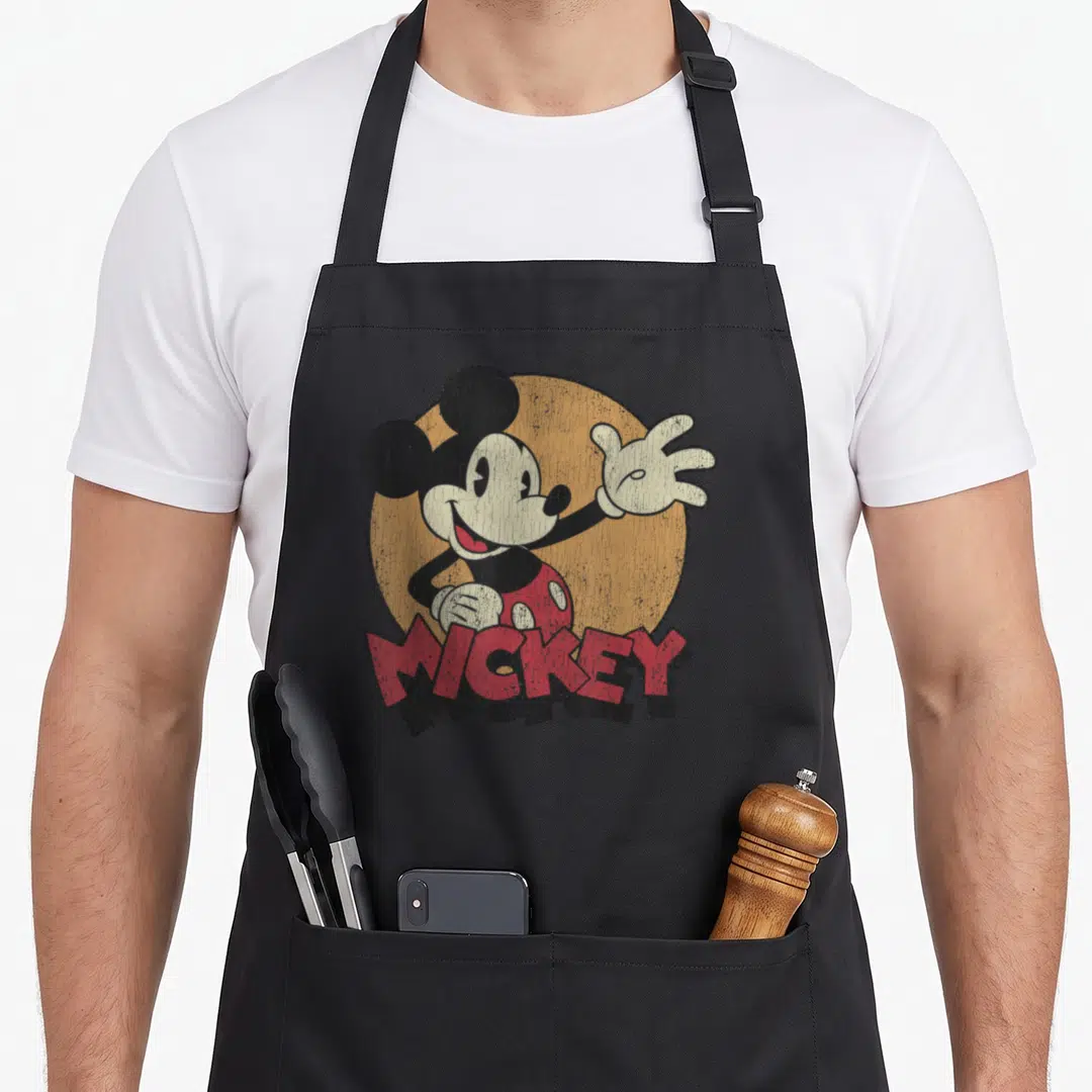 Distressed best friend aprons - Retro Mickey Mouse waving in front of tan circle with red MICKEY text overlay — shown on a black cotton canvas apron against a white background