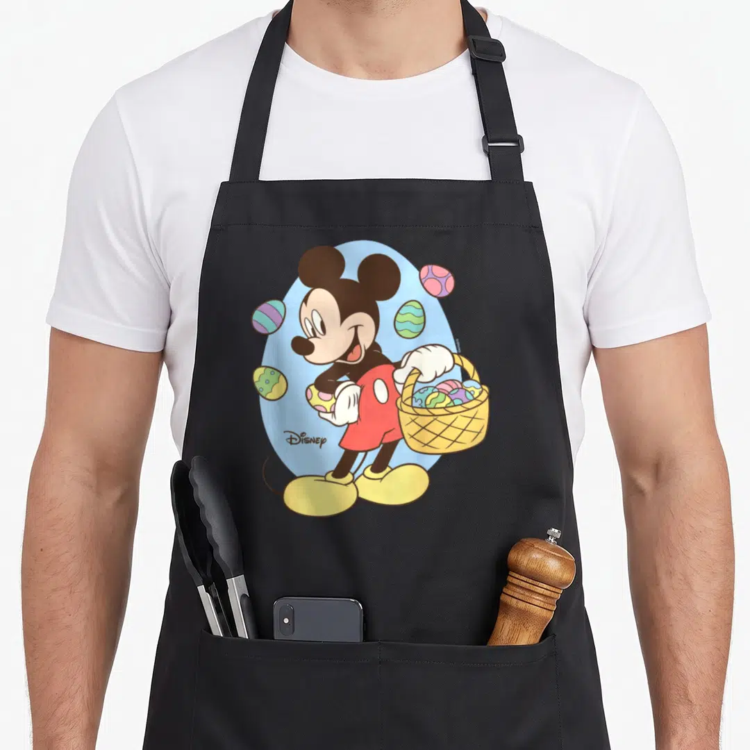 Cool easter basket apron - Mickey Mouse holding basket and egg, cartoon style, blue oval, red shorts, yellow shoes — shown on a black cotton canvas apron against a white background