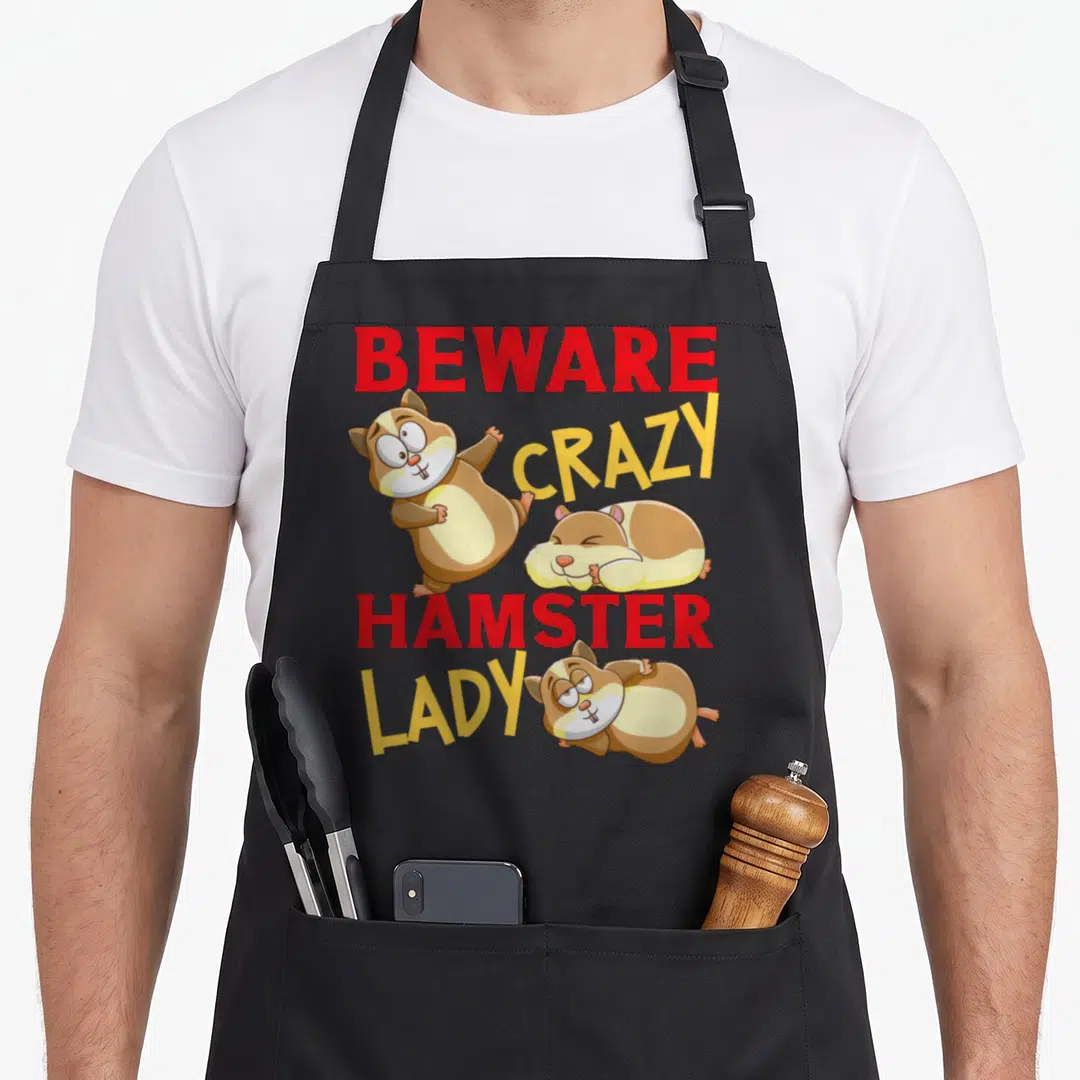 Comfort crazy hamster lady apron - Stacked text BEWARE CRAZY HAMSTER LADY with three cartoon hamsters in brown and beige — shown on a black cotton canvas apron against a white background