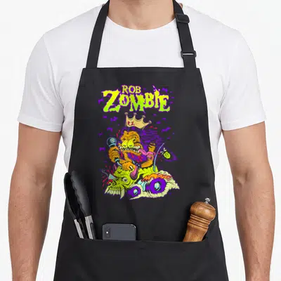 Rob king apron - Lime green ROB ZOMBIE text above an orange monster with a crown riding a purple motorcycle surrounded — shown on a black cotton canvas apron against a white background