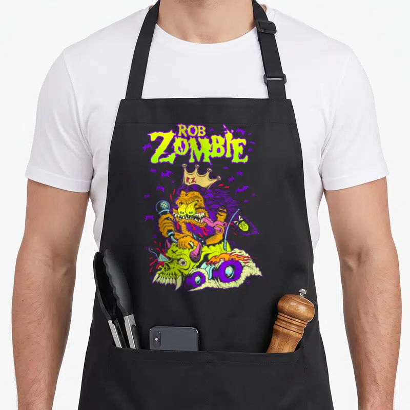 Rob king apron - Lime green ROB ZOMBIE text above an orange monster with a crown riding a purple motorcycle surrounded — shown on a black cotton canvas apron against a white background