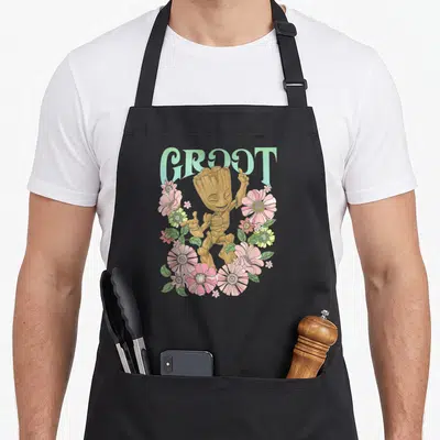 Guardian floral apron - GROOT text above dancing cartoon character surrounded by pink green and blue flowers — shown on a black cotton canvas apron against a white background