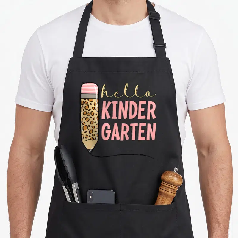 Pencil hello apron - Leopard print pencil with pink eraser and stacked hello KINDER GARTEN text in pink and tan — shown on a black cotton canvas apron against a white background