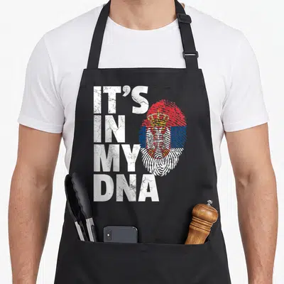 Serbian country apron - Distressed IT'S IN MY DNA text next to a Serbian flag and coat of arms fingerprint — shown on a black cotton canvas apron against a white background