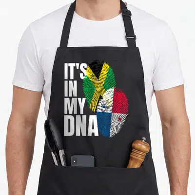 Panamanian heritage aprons - Stacked white text IT'S IN MY DNA beside two overlapping fingerprints filled — shown on a black cotton canvas apron against a white background