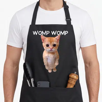 Womp cat apron - Orange and white kitten photo with arched WOMP WOMP text above — shown on a black cotton canvas apron against a white background