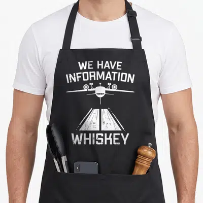 Boredkoalas aviation apron - White distressed We Have Information Whiskey text with airplane and runway graphic — shown on a black cotton canvas apron against a white background