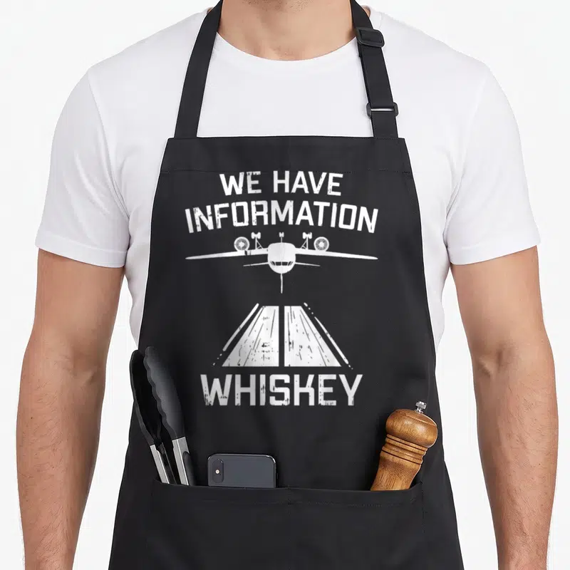Boredkoalas aviation apron - White distressed We Have Information Whiskey text with airplane and runway graphic — shown on a black cotton canvas apron against a white background