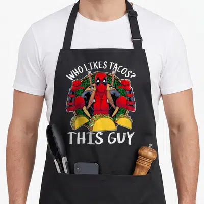 Thumb taco apron - Deadpool with three tacos and arched white text on black bib — shown on a black cotton canvas apron against a white background