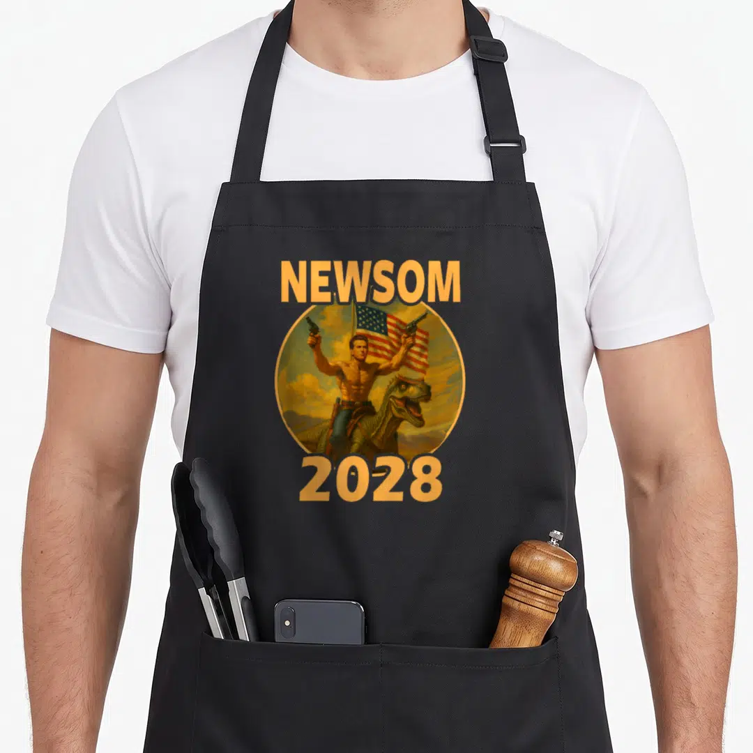 Gavin patriotic apron - Newsom 2028 text above and below a man riding a dinosaur holding two guns inside a circular — shown on a black cotton canvas apron against a white background
