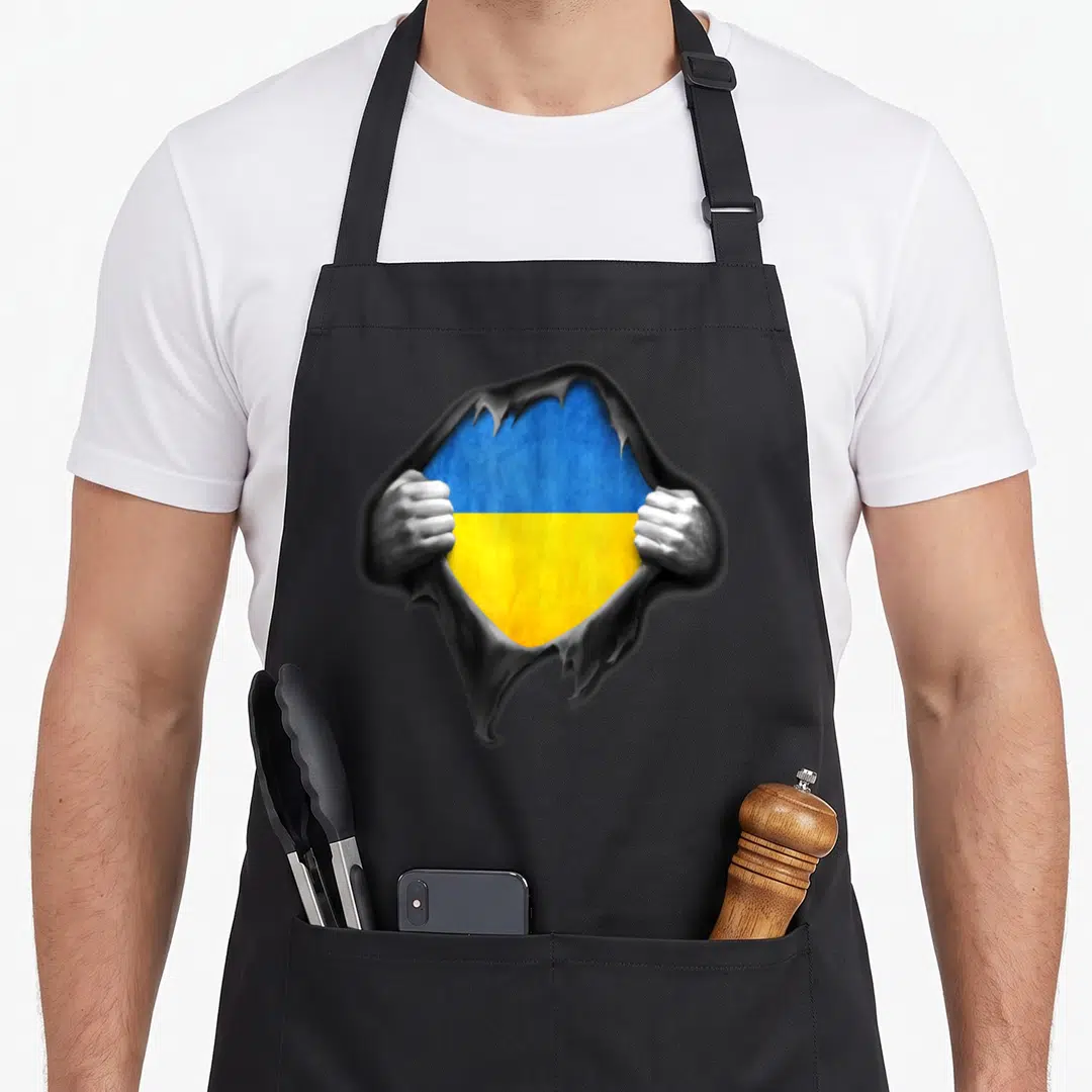 Ukraine pride ukrainian aprons - Two hands tear grey surface to reveal blue and yellow flag — shown on a black cotton canvas apron against a white background