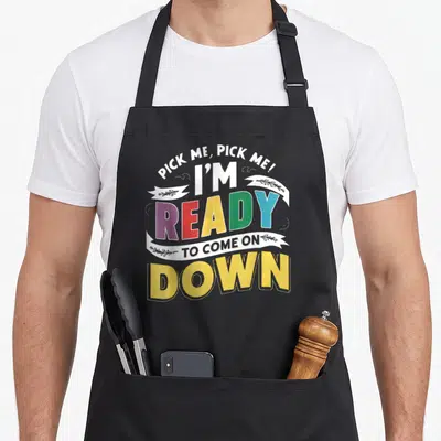 Pick making quotes apron - Stacked colorful text reading Pick Me I'm Ready To Come On Down with ribbon details — shown on a black cotton canvas apron against a white background