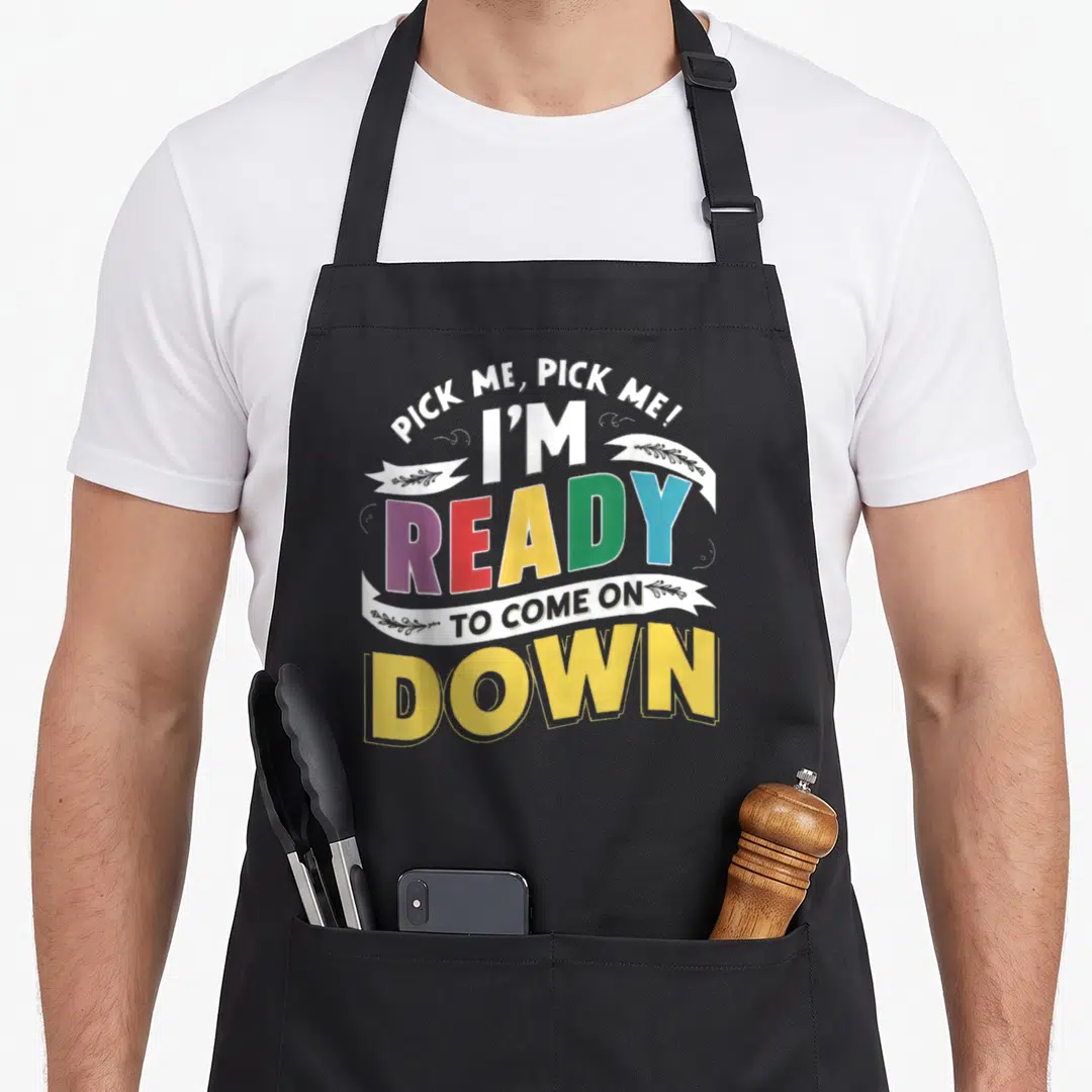 Pick making quotes apron - Stacked colorful text reading Pick Me I'm Ready To Come On Down with ribbon details — shown on a black cotton canvas apron against a white background