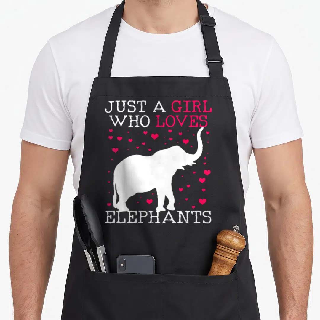 Cute elephant print apron - White elephant silhouette surrounded by pink hearts and text reading JUST A GIRL WHO LOVES — shown on a black cotton canvas apron against a white background