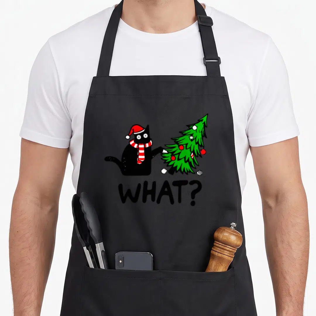 Pushing black cat apron - Cartoon black cat in Santa hat pushing green Christmas tree with text WHAT? — shown on a black cotton canvas apron against a white background