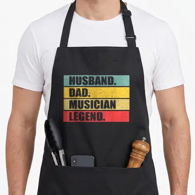 Musician father day apron - Stacked grey text reading husband dad musician legend on teal yellow beige and red — shown on a black cotton canvas apron against a white background