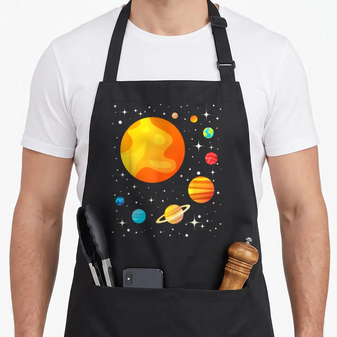 Astronomer science apron - Large orange sun and multiple planets with rings and stars on gray background — shown on a black cotton canvas apron against a white background