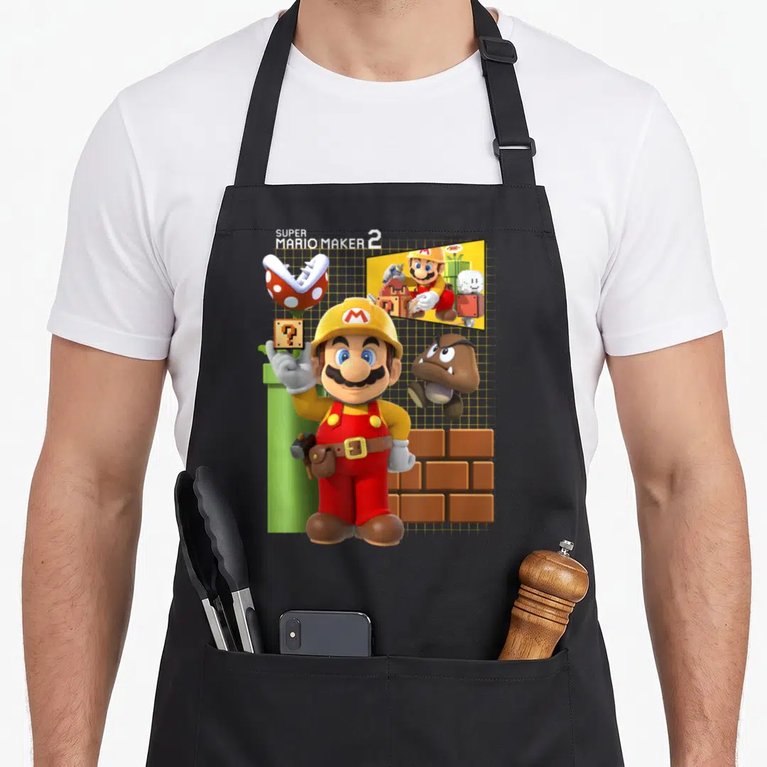 Game maker apron - Mario in hard hat with Piranha Plant, Goomba, brick wall, and level screen under SUPER MARIO MAKER 2 — shown on a black cotton canvas apron against a white background