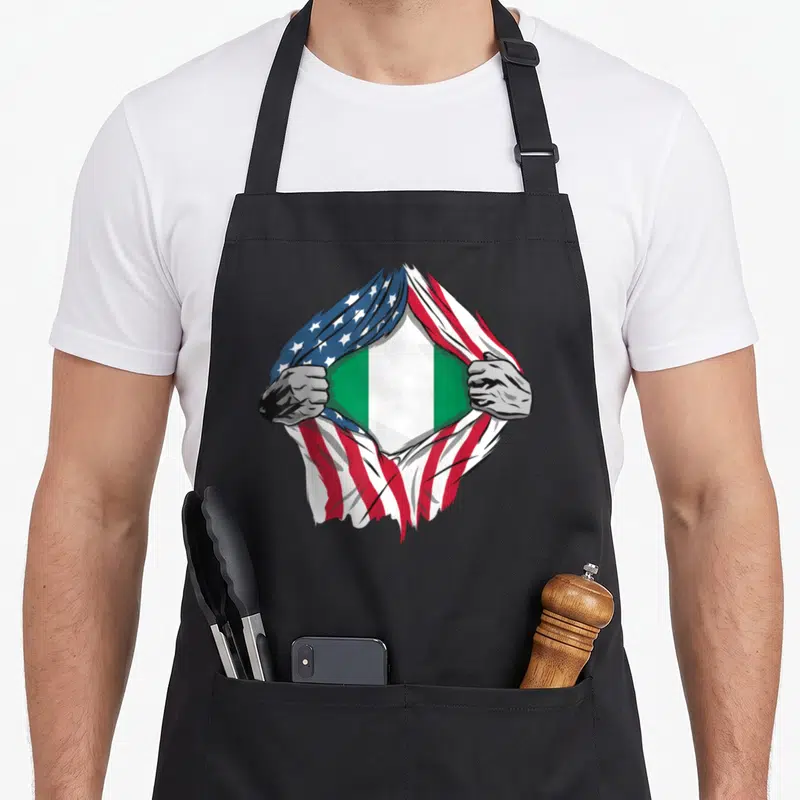 Inside american flag apron - Two grey hands tear red white blue flag to reveal green white flag — shown on a black cotton canvas apron against a white background