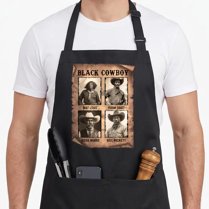 Melanin western aprons - Torn paper graphic with four sepia cowboy portraits labeled Nat Love, Isom Dart, Bose Ikard — shown on a black cotton canvas apron against a white background