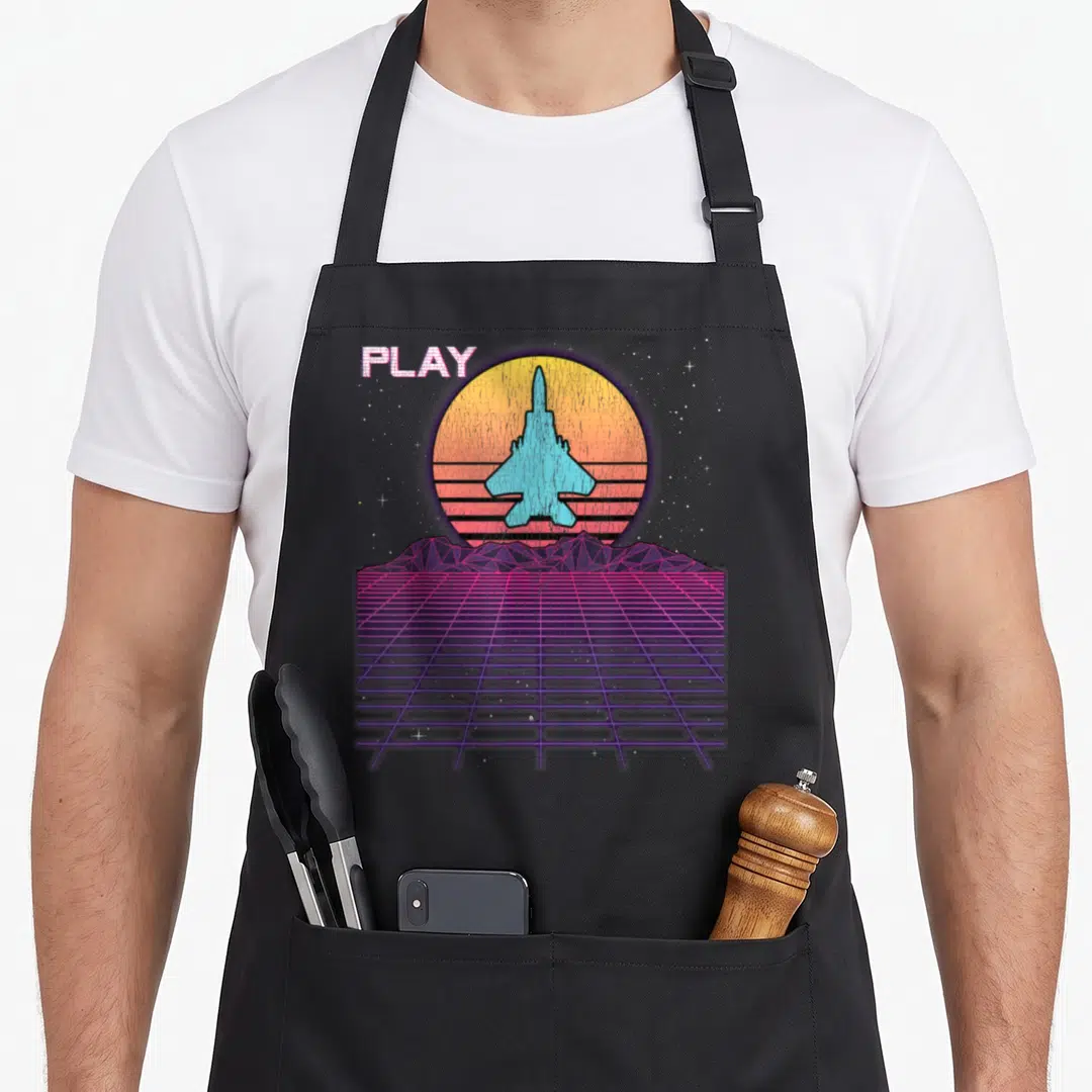 Raptor f18 apron - Retro fighter jet over striped sun with PLAY text and purple grid landscape — shown on a black cotton canvas apron against a white background