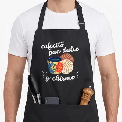 Pan mexican apron - Coffee mug with flowers and two conchas under white text — shown on a black cotton canvas apron against a white background