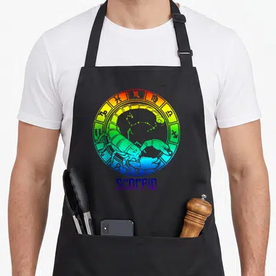 Sign star birthday apron - Rainbow gradient zodiac wheel with cartoon scorpion, constellation, and SCORPIO text below — shown on a black cotton canvas apron against a white background
