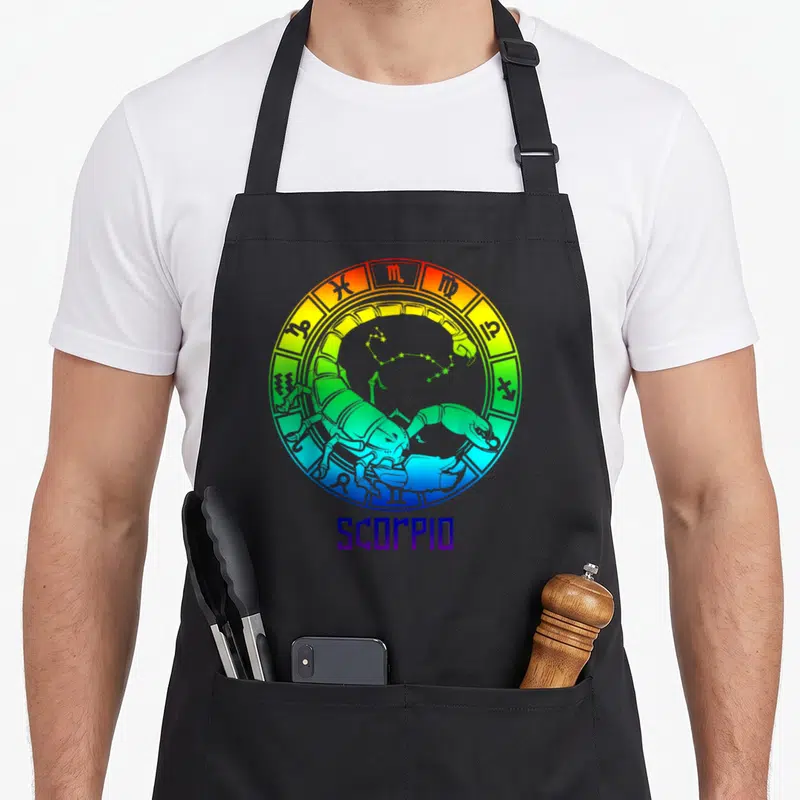 Sign star birthday apron - Rainbow gradient zodiac wheel with cartoon scorpion, constellation, and SCORPIO text below — shown on a black cotton canvas apron against a white background