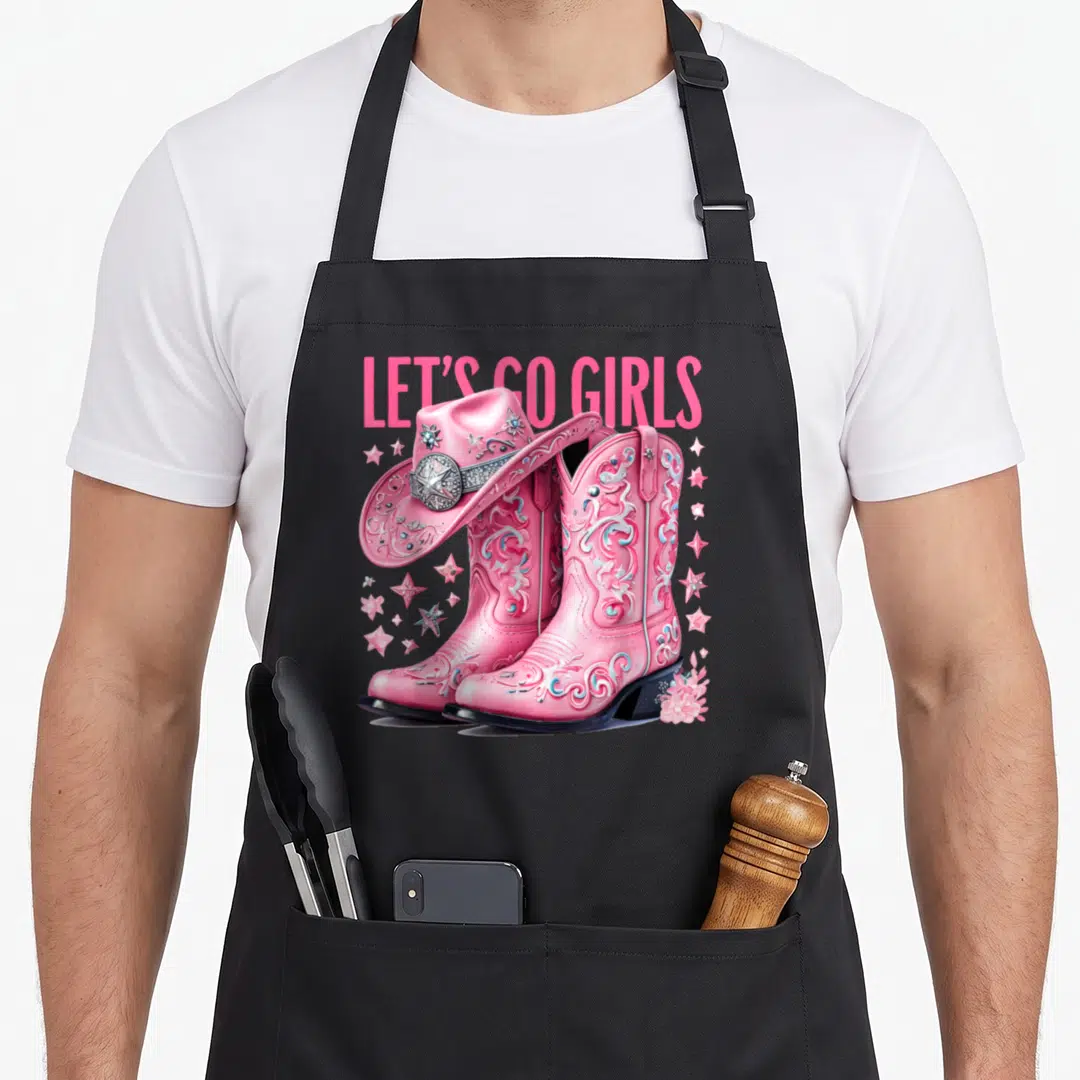 Coquette country apron - Pink cowgirl boots with cowboy hat, stars, flower, and LET'S GO GIRLS text — shown on a black cotton canvas apron against a white background