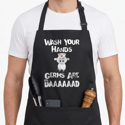 Germ nurse apron - Cartoon sheep in nurse hat between wash hands and germs are baaaaad text — shown on a black cotton canvas apron against a white background