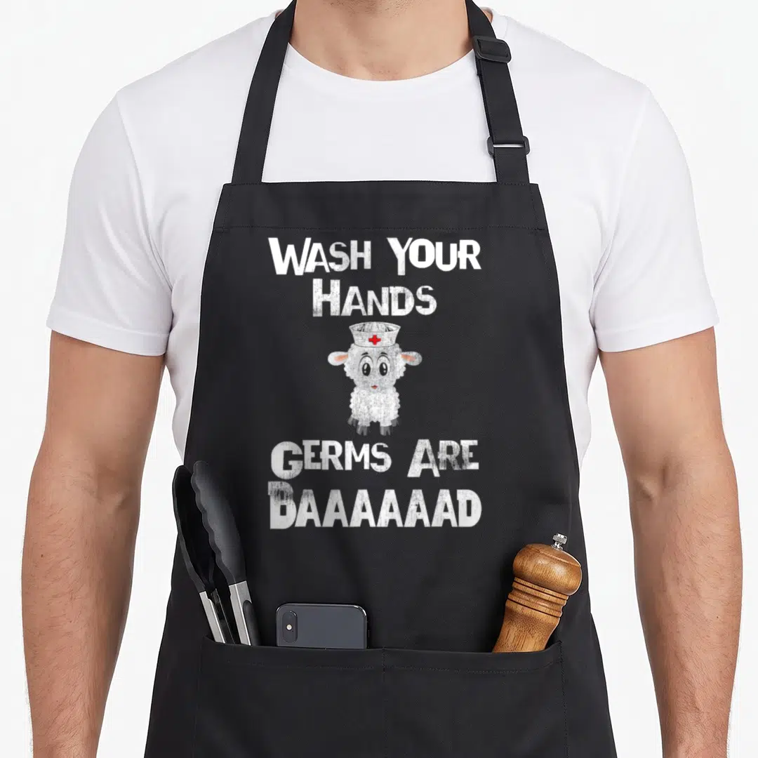 Germ nurse apron - Cartoon sheep in nurse hat between wash hands and germs are baaaaad text — shown on a black cotton canvas apron against a white background