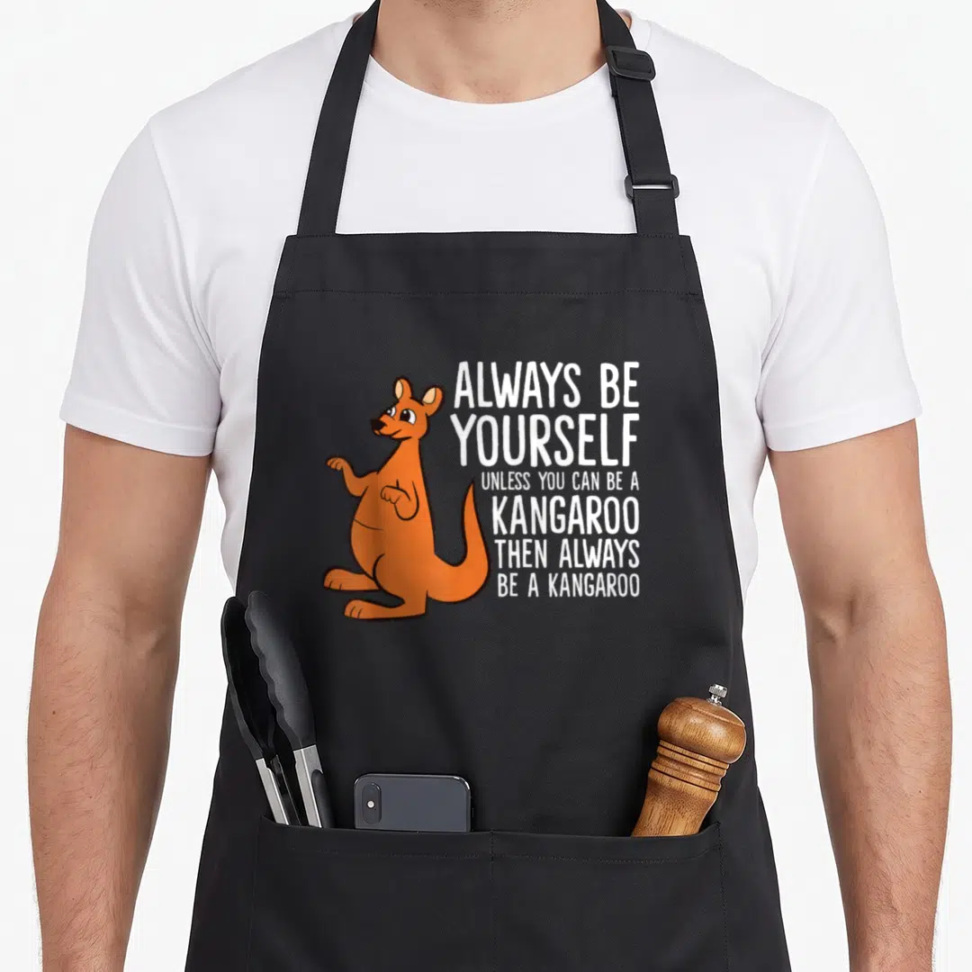 Alway kangaroo apron - Orange cartoon kangaroo standing next to stacked white text reading Always Be Yourself Unless — shown on a black cotton canvas apron against a white background