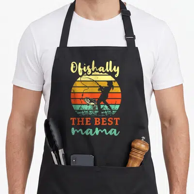 Fisherwoman fishing aprons - Retro sunset graphic with fishing woman silhouette and Ofishally THE BEST mama text — shown on a black cotton canvas apron against a white background