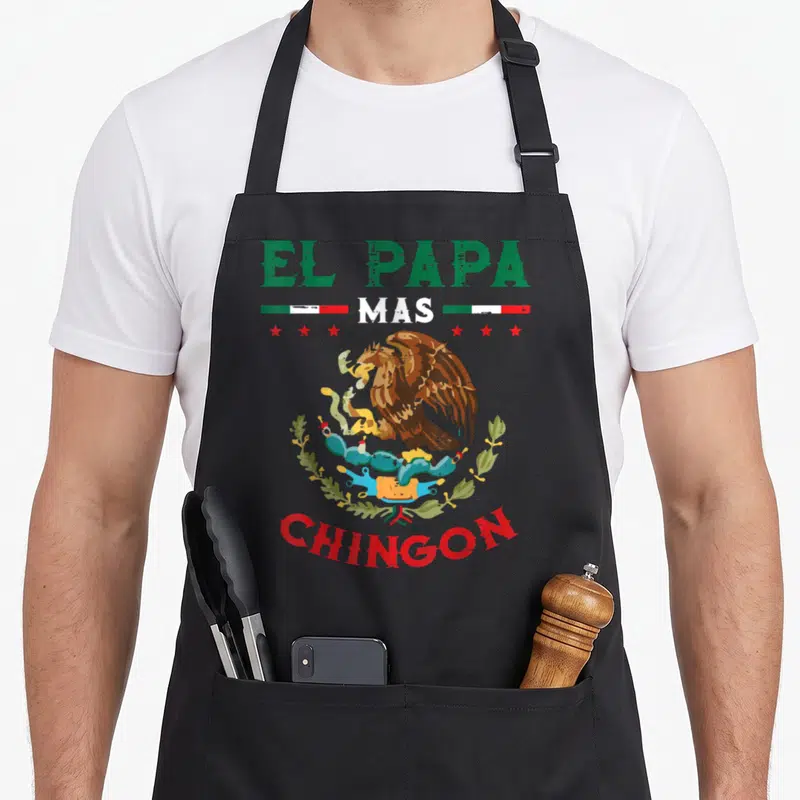 Mas father day apron - El Papa Mas Chingon text surrounding a distressed Mexican coat of arms in green white and red — shown on a black cotton canvas apron against a white background