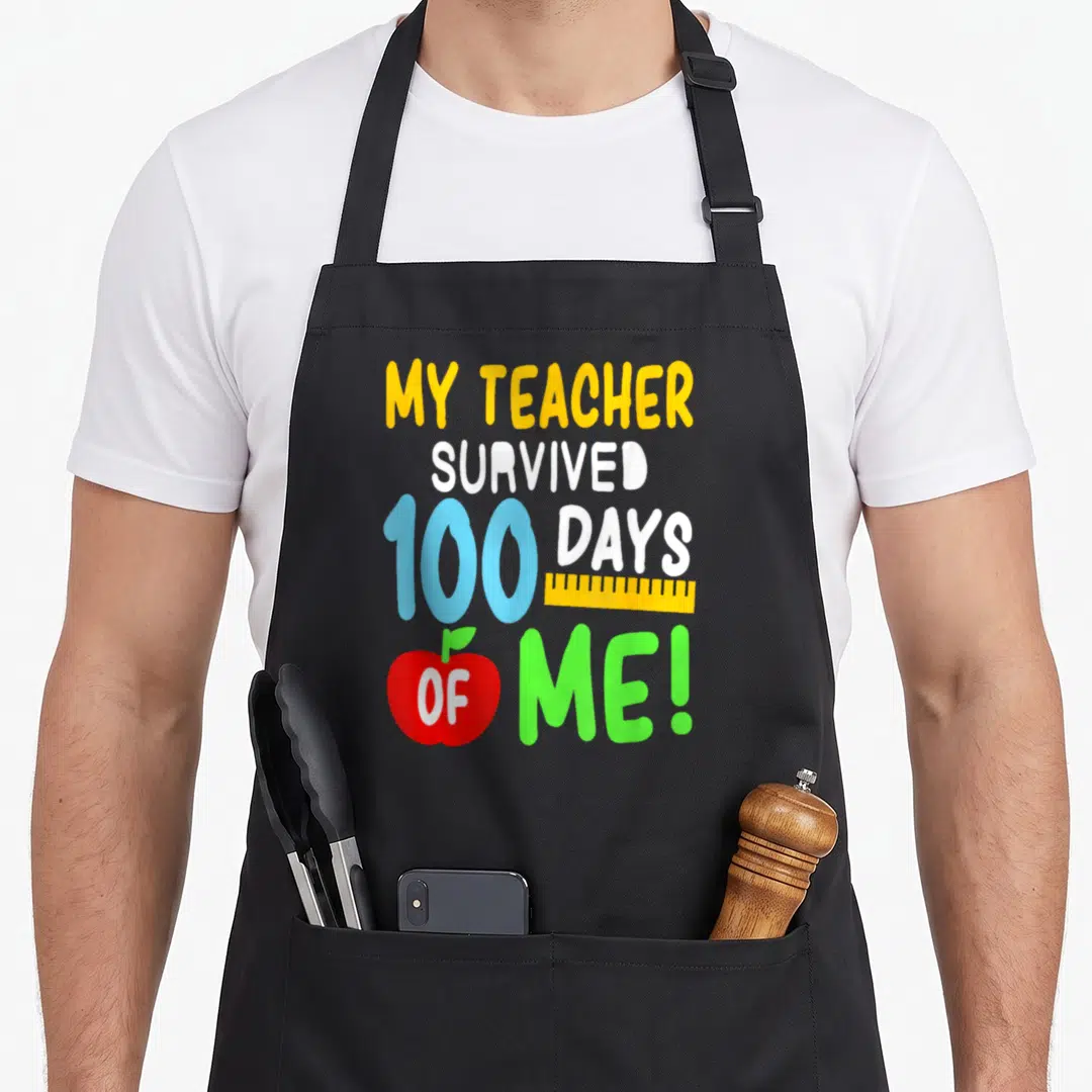 Survived school teacher apron - Stacked colorful text My Teacher Survived 100 Days Of Me with yellow ruler and red — shown on a black cotton canvas apron against a white background