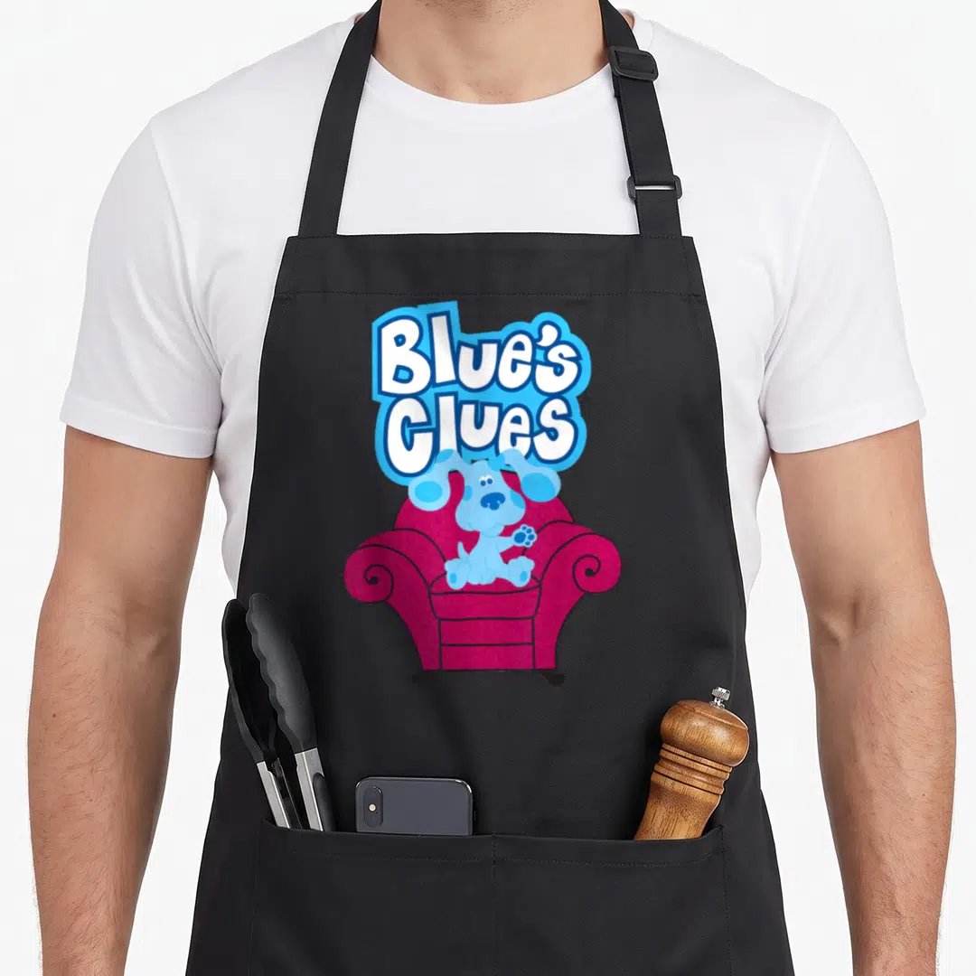 Blue couch apron - Cartoon blue dog sitting in magenta armchair under stacked Blue's Clues logo — shown on a black cotton canvas apron against a white background