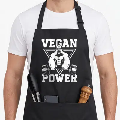 Workout vegan apron - White gorilla lifting barbell inside triangle with VEGAN POWER text — shown on a black cotton canvas apron against a white background