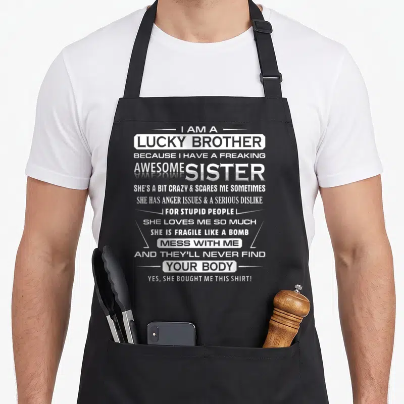 Brother christmas apron - White stacked typography reading I Am A Lucky Brother Because I Have A Freaking Awesome Sister — shown on a black cotton canvas apron against a white background