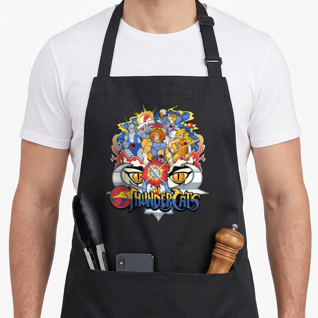 Badge shot apron - THUNDERCATS text below characters clustered over a pair of large eyes in blue red yellow orange — shown on a black cotton canvas apron against a white background