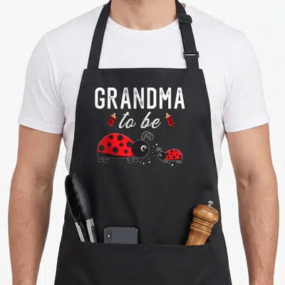 Ladybug grandma apron - GRANDMA to be text with two red baby bottles and a large ladybug facing a small one — shown on a black cotton canvas apron against a white background