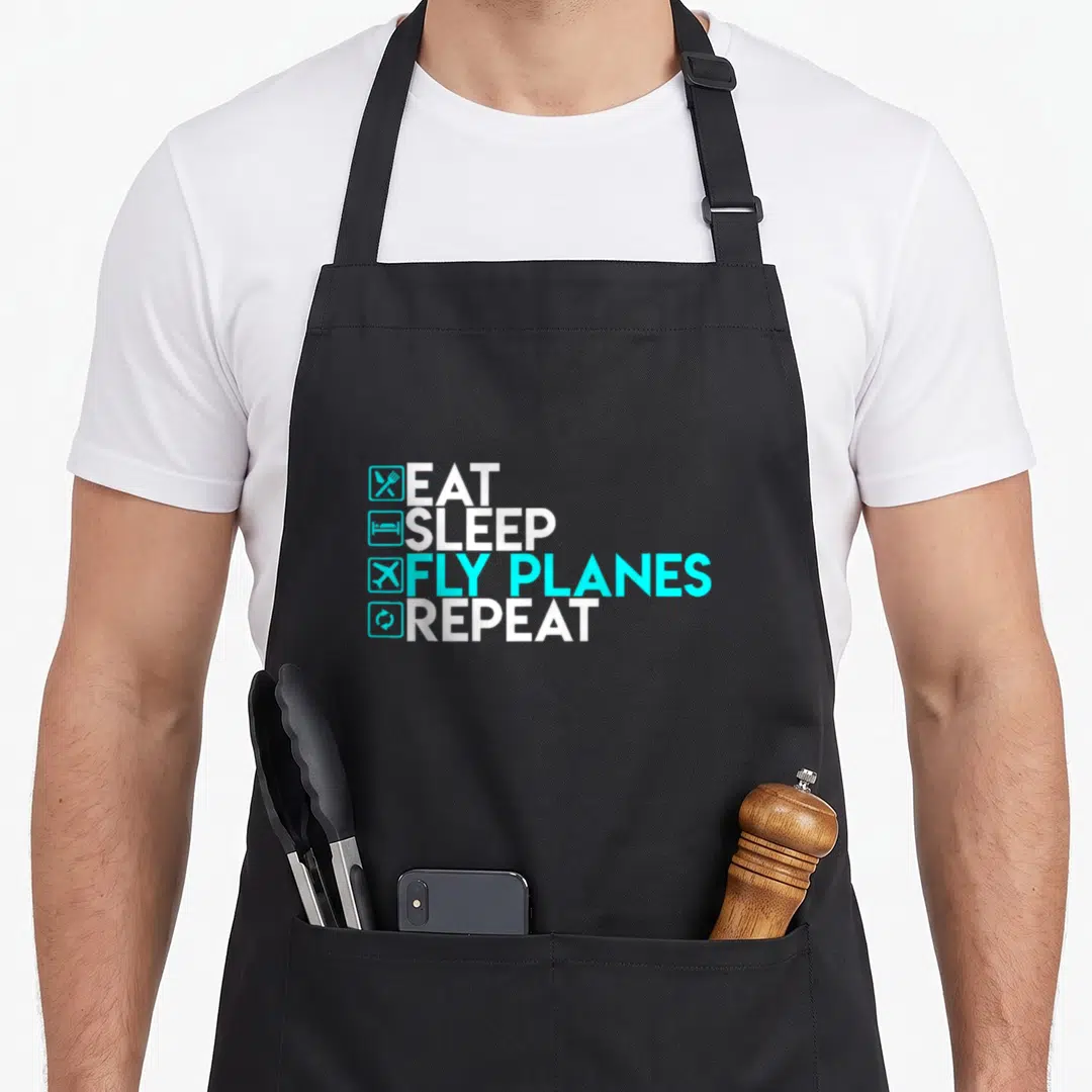 Eat trendy apron - Stacked white and cyan text EAT SLEEP FLY PLANES REPEAT with four square icons — shown on a black cotton canvas apron against a white background