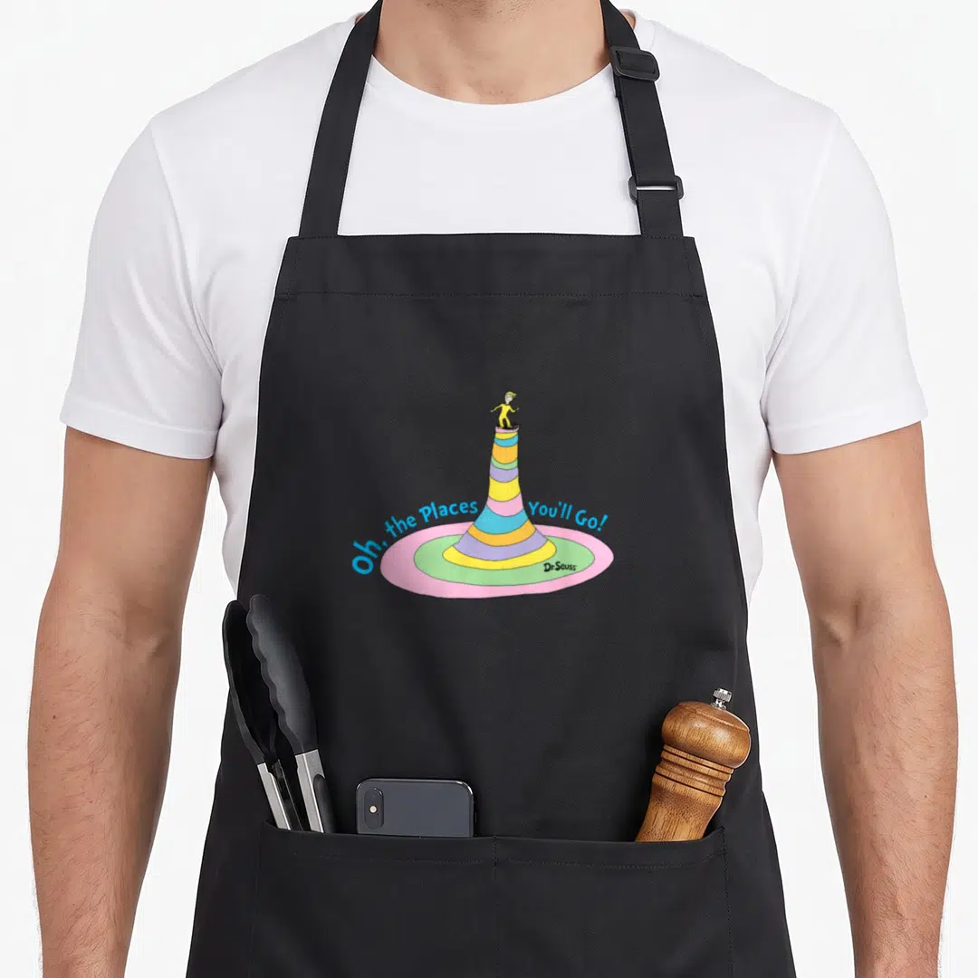 Balancing you youll apron - Cartoon character standing on tall striped cone with arching blue text Oh the Places You'll — shown on a black cotton canvas apron against a white background