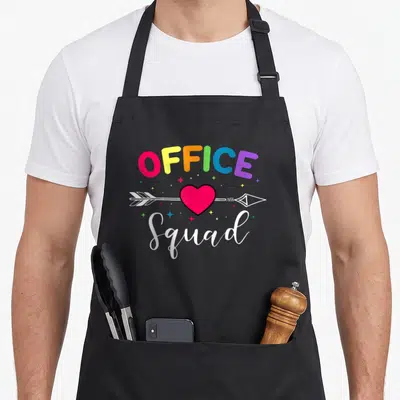 Administrative assistant office apron - Rainbow OFFICE text, red heart pierced by white arrow, white Squad script — shown on a black cotton canvas apron against a white background