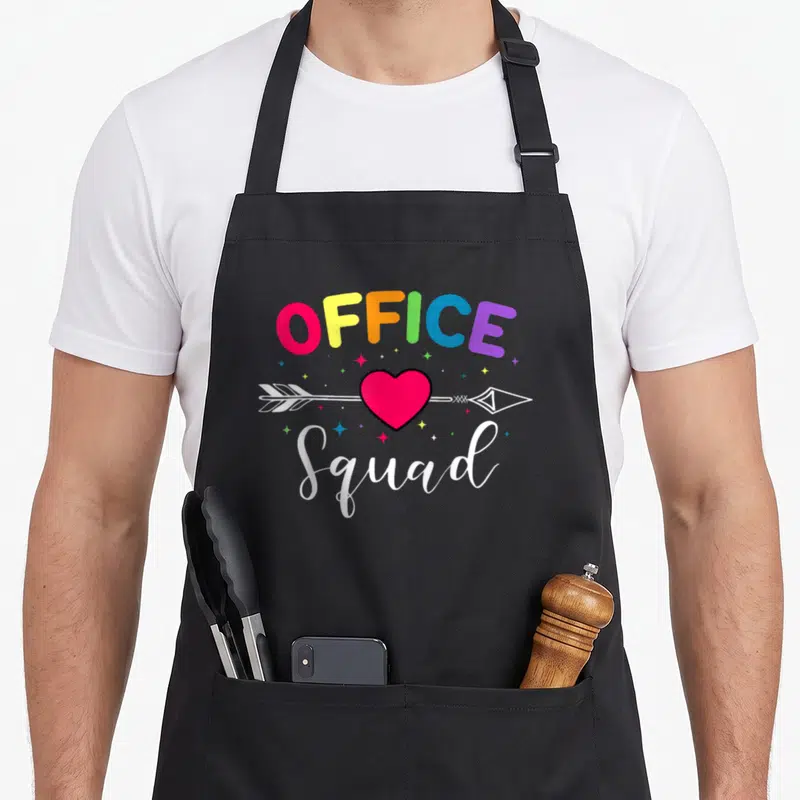 Administrative assistant office apron - Rainbow OFFICE text, red heart pierced by white arrow, white Squad script — shown on a black cotton canvas apron against a white background