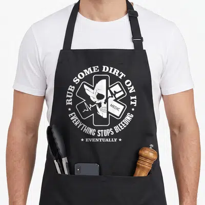 Rub emt apron - White medical cross with skull, bandage, and Rub Some Dirt On It text — shown on a black cotton canvas apron against a white background