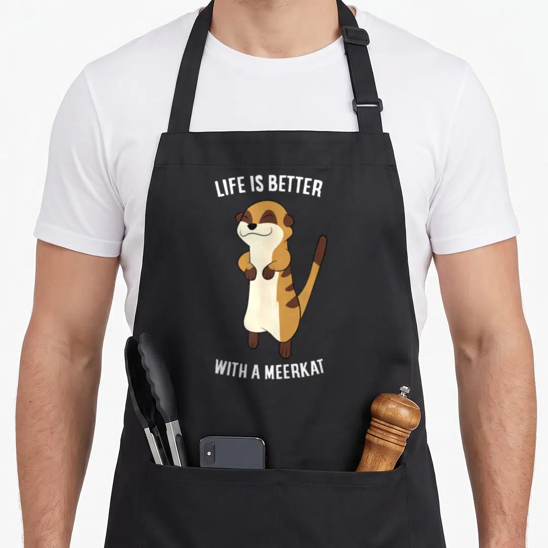 Better meerkat apron - Cartoon meerkat standing between LIFE IS BETTER and WITH A MEERKAT text in white, brown, and tan — shown on a black cotton canvas apron against a white background
