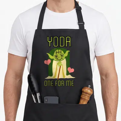 Yoda valentine's day apron - Cartoon Yoda holding a cane between two pink hearts with text YODA and ONE FOR ME — shown on a black cotton canvas apron against a white background